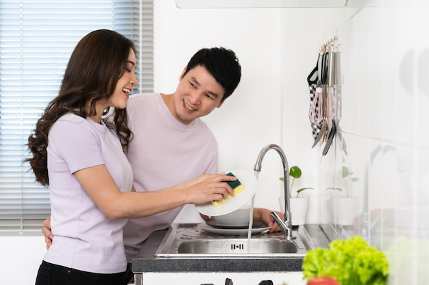 Happy couple washing dishes together in the sink in the kitchen at home