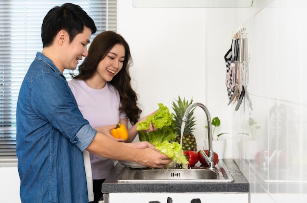 Happy couple washing vegetables in the sink in the kitchen at home cooking together