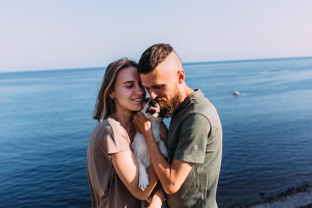 Happy couple with favourite pet young man and woman have walk near sea