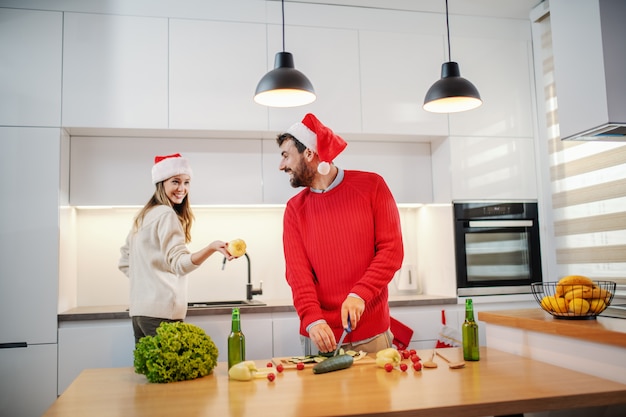 Happy couple with santa hats on heads preparing healthy food for New Year's eve