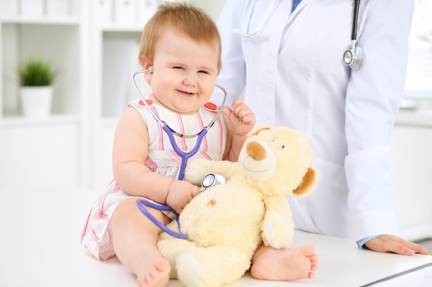 Happy cute baby at health exam at doctor's office Toddler girl is sitting and keeping stethoscope and teddy bear