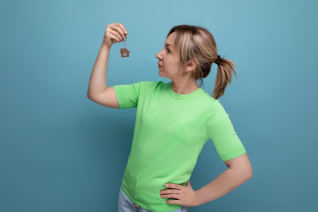 Happy cute blond woman in casual look holding new apartment keychain on blue background