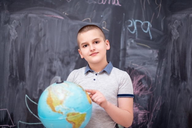 happy cute boy learning about the world using globe of earth while standing in front of black chalkboard