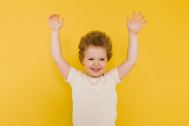 Happy cute fouryearold kid in a light Tshirt raising his hands up looks at you with interest