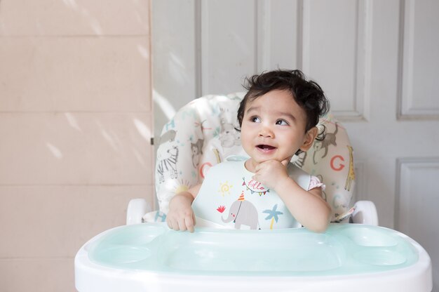 happy cute little asian baby siting on baby dining table smile and looking out with copy space