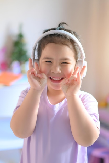 Happy cute little asian girl  listening music in headphones . music, technology and people concept.