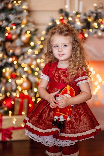 Happy cute little blonde girl with long hair in a red dress, waiting for Christmas