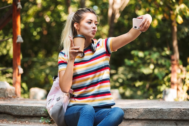 Happy cute young girl take selfie by mobile phone holding coffee.