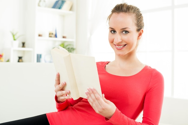 Happy cute young woman in home reading book