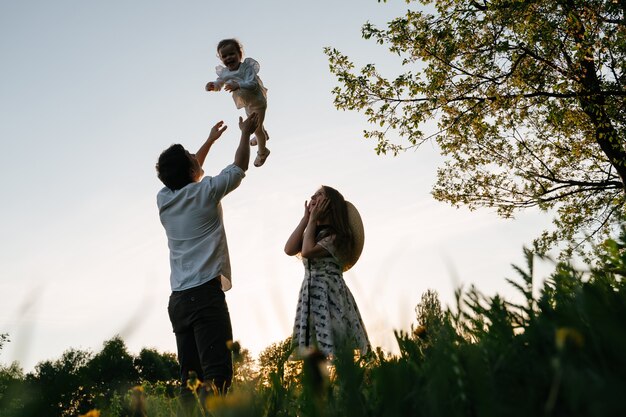 Happy dad happily throws the child to a girl playing with her mom looks frightened at her daughter a family walk on a green lawn in the field