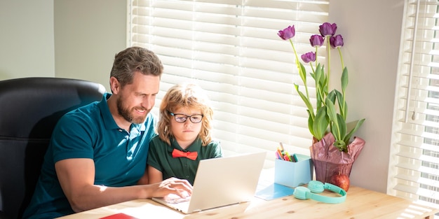 Happy dad helping his school son child in glasses study with computer at home parenthood