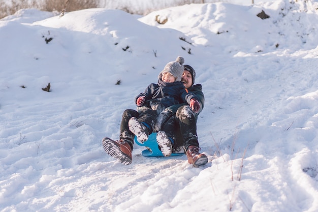 Happy dad and little boy playing with snow sled