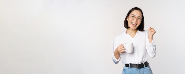 Happy dancing woman drinking coffee or tea from mug Korean girl with cup standing over white background