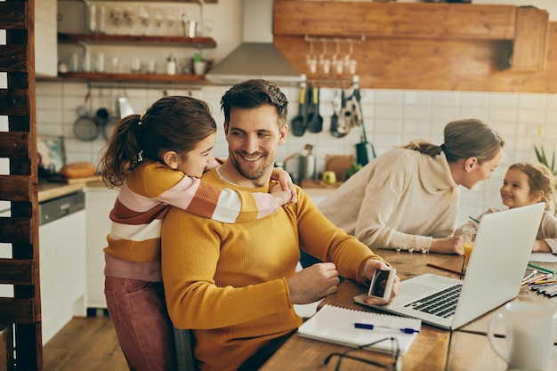 Happy daughter embracing her father who is working on laptop at home