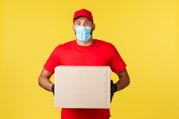 Happy delivery man wearing a face mask holding a box