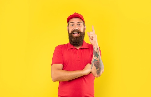 Happy deliveryman in casual red cap and tshirt keeping finger raised yellow background idea