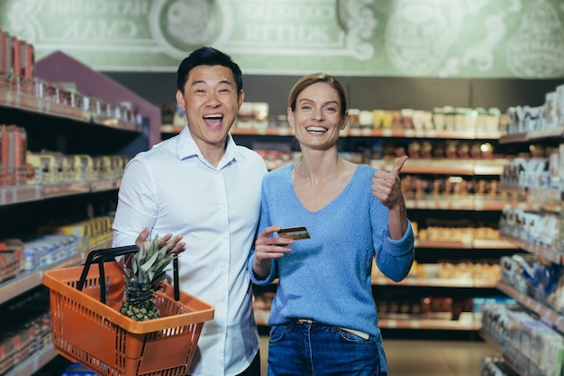 Happy diverse family couple man and woman shoppers in supermarket looking at camera and smiling