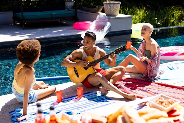 Happy diverse group of friends having pool party, playing guitar in garden. Lifestyle, friendship, party and summer.