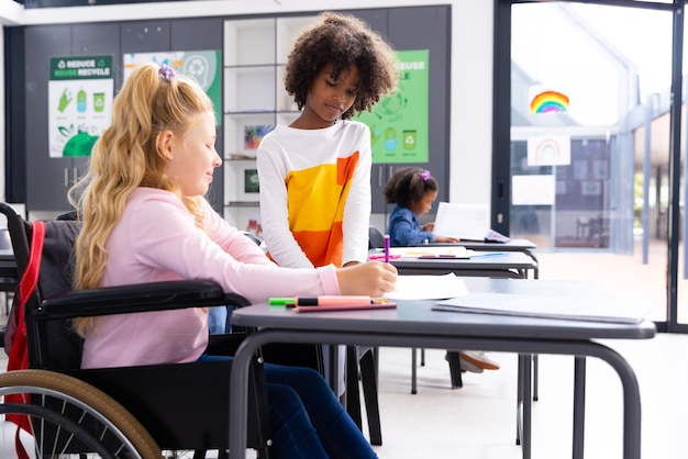 Photo happy diverse schoolgirl in wheelchair with her friend in school classroom