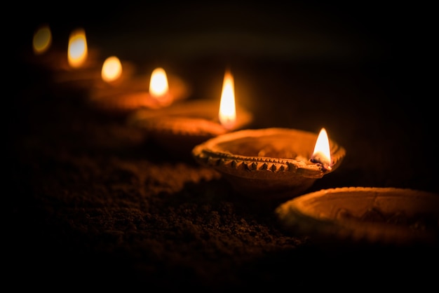 Happy Diwali - many Terracotta diya or oil lamps arranged over clay surface or ground in one line or curved or zigzag form, selective focus