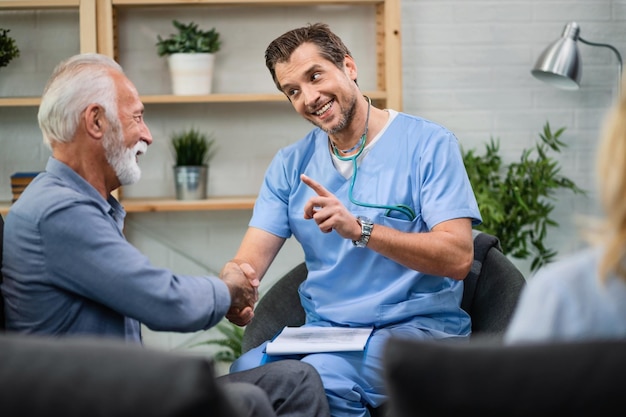 Happy doctor communicating with senior man while shaking hands with him during a home visit