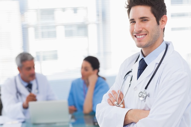 Happy doctor looking at camera with colleagues behind