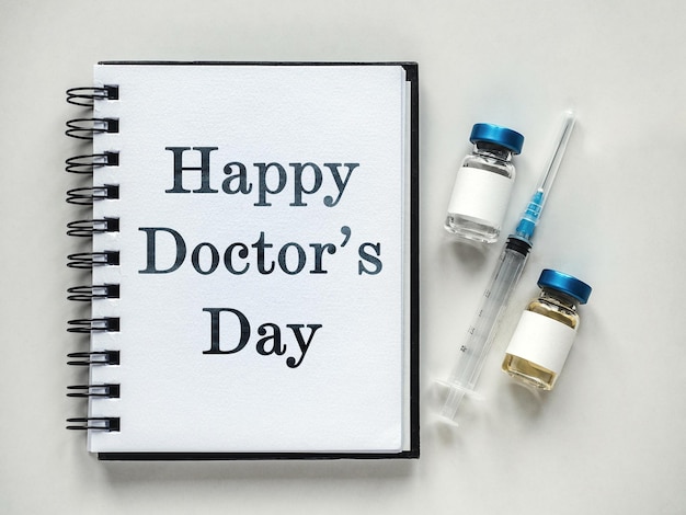 Photo happy doctor's day. syringes, injection vials and a notepad lying on the table. close-up, indoors, view from above. day light, studio photo. healthcare concept