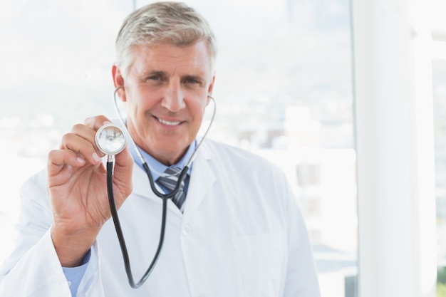 Happy doctor smiling at camera and showing his stethoscope 