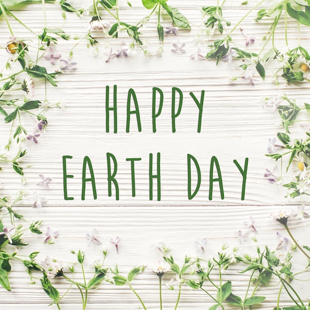 Happy earth day text sign on beautiful lilac and daisy flowers on rustic white wooden background top view greeting card environmental concept earth day save environment eco