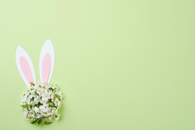 Happy Easter Bunny rabbit ears made of pink paper and round bouquet of springs fresh cherry or apple blossoms on green background Easter greeting card with copy space Happy Easter concept Mock up