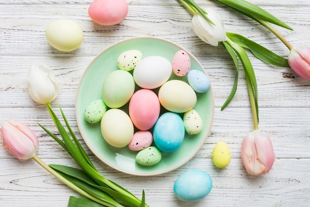 Happy Easter composition Easter eggs in basket on colored table with yellow Tulips Natural dyed colorful eggs background top view with copy space