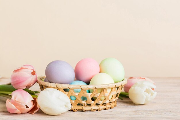 Happy Easter composition Easter eggs in basket on colored table with yellow Tulips Natural dyed colorful eggs background with copy space