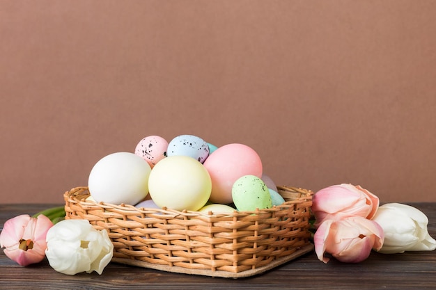 Happy Easter composition Easter eggs in basket on colored table with yellow Tulips Natural dyed colorful eggs background with copy space