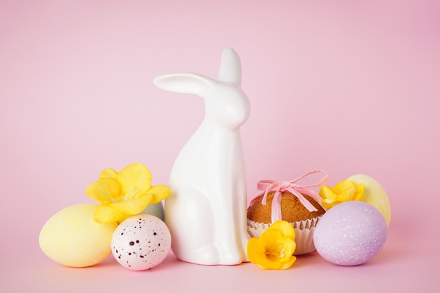 Happy Easter concept. Easter cake, Easter bunny and eggs with flowers on a pink background.