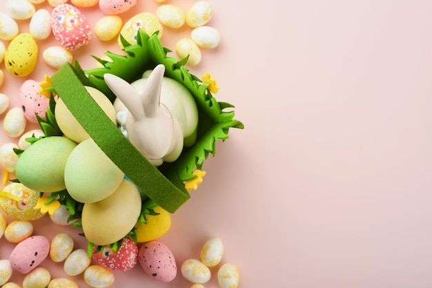 Happy Easter Easter eggs and rabbit in green basket on pink background with white and yellow roses Spring Happy Easter holiday card Easter background with copy space Top view