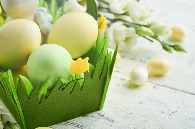 Happy Easter Easter eggs and rabbit in green basket on white old wooden table with white and yellow roses Spring Happy Easter holiday card Easter background with copy space Top view