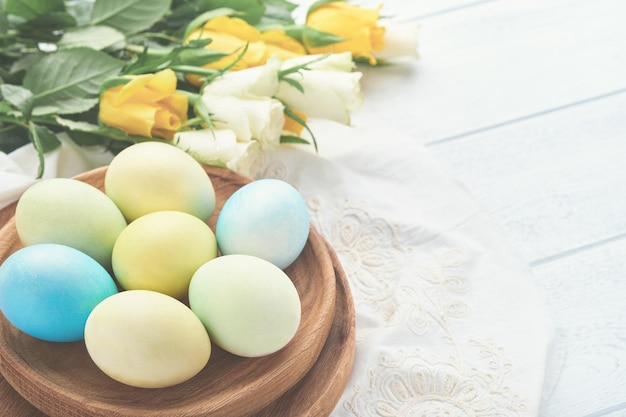 Happy Easter Easter eggs on rustic table with white and yellow roses Natural dyed colorful eggs in wooden plate and spring flowers in rustic room Toned image Easter background with copy space