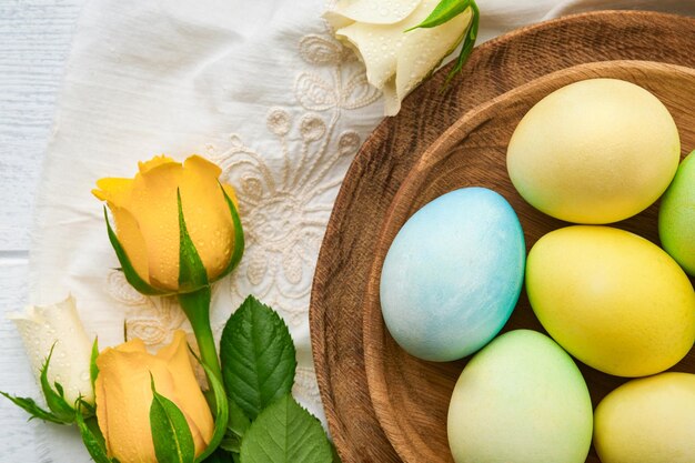 Happy Easter Easter eggs on rustic table with white and yellow roses Natural dyed colorful eggs in wooden plate and spring flowers in rustic room Toned image Easter background with copy space