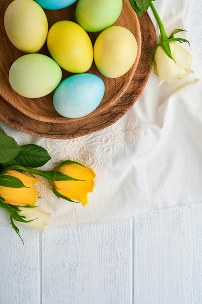 Happy Easter Easter eggs on rustic table with white and yellow roses Natural dyed colorful eggs in wooden plate and spring flowers in rustic room Toned image Easter background with copy space