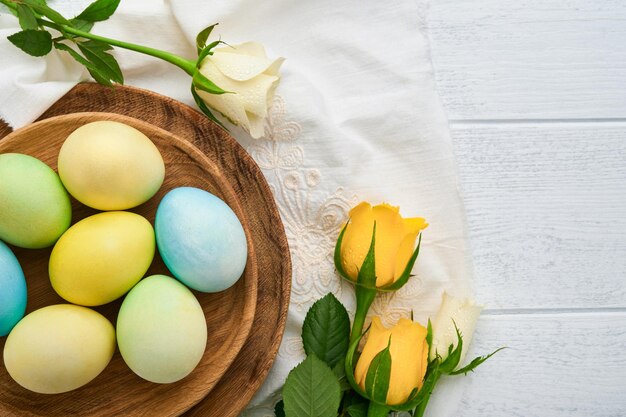 Happy Easter Easter eggs on rustic table with white and yellow roses Natural dyed colorful eggs in wooden plate and spring flowers in rustic room Toned image Easter background with copy space