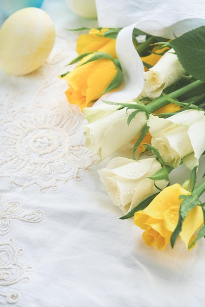 Happy Easter Easter eggs on rustic table with white and yellow roses Natural dyed colorful eggs in wooden plate and spring flowers in rustic room Toned image Easter background with copy space