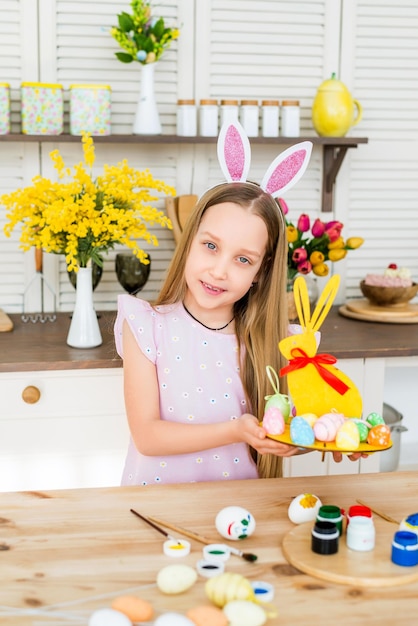 Happy Easter. A happy child is preparing for Easter. The girl holds a stand in the form of a rabbit with colored eggs..