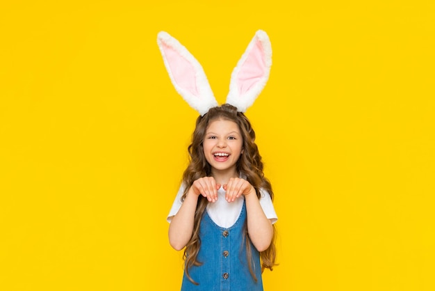 Happy Easter holiday A beautiful little girl with rabbit ears on her head celebrating a spring day The child depicts a rabbit on a yellow isolated background