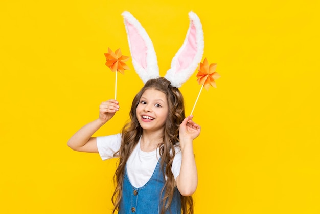 Happy Easter holiday A beautiful little girl with rabbit ears on her head celebrating a spring day A child in a sundress holds origami flowers on a yellow isolated background