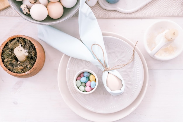 Happy easter holiday in springtime season festive home decor traditional food white beige chicken egg wrapped in pale blue cloth like rabbit or bunny ears in plate and small candy eggs on table