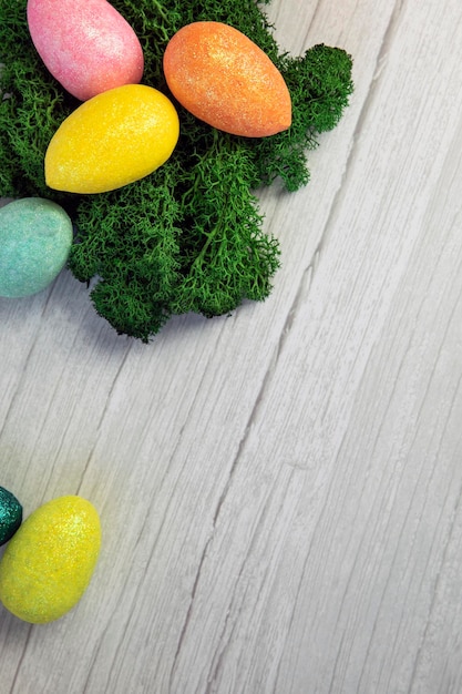 Happy Easter holliday concept, colorful easter eggs with green moss on white wooden background texture top view, copy space, bright colors