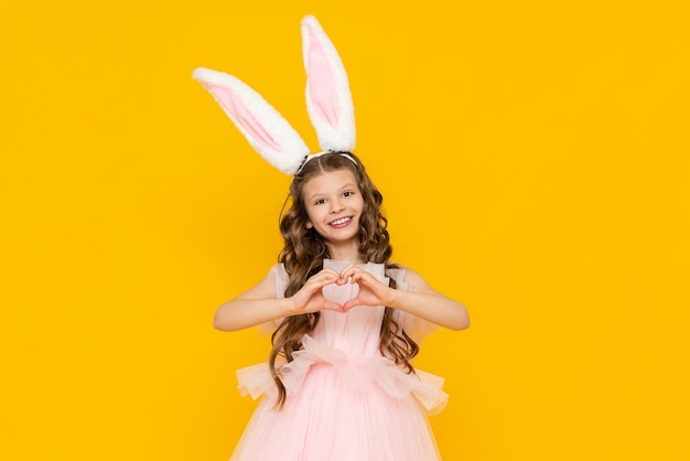 Happy Easter A little girl dressed as a rabbit celebrates a spring holiday A charming smiling child in a beautiful dress with long ears on a yellow isolated background