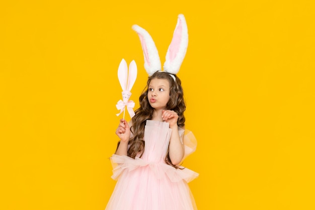 Happy Easter A little girl dressed as a rabbit celebrates a spring holiday A charming smiling child in a beautiful dress with long ears on a yellow isolated background