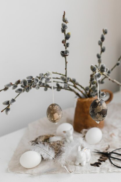 Happy Easter Natural eggs bunny figurines feathers nest willow branches in vase on table