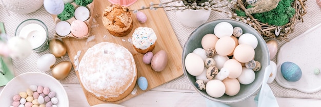 Happy easter and spring holidays time festive tablescape set decor traditional dinner food easter eggs and baked cakes on table at home pale pop pastel blue and pink color top view banner